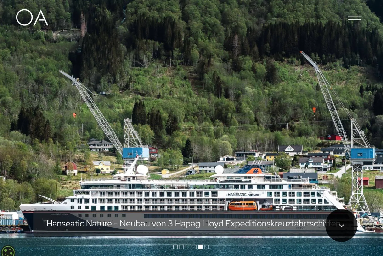 Hanseatic Nature Expeditionskreuzfahrtschiff neben Kränen vor bewaldetem Hang mit Häusern.