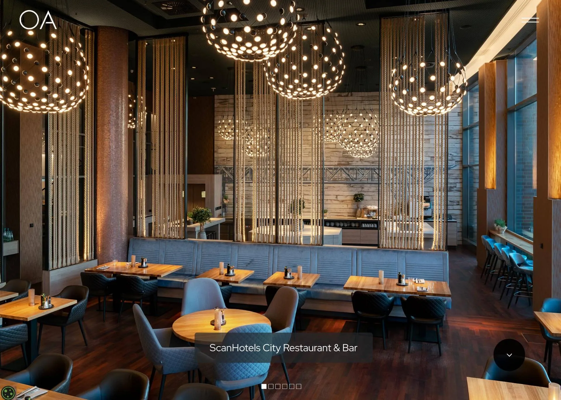 Modernes Restaurant mit Holztischen, blauen Sesseln, großen runden Lampen und einem Lounge-Bereich.